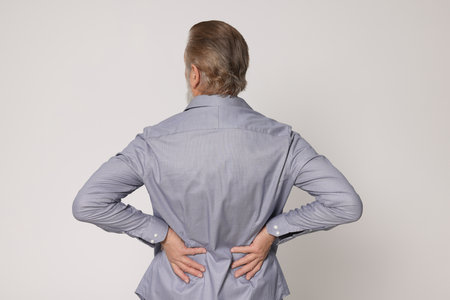Senior man suffering from pain in back on light gray background. Arthritis symptoms