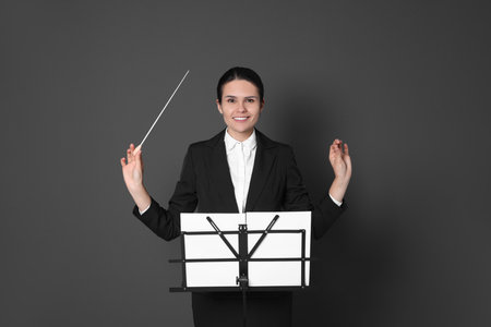 Happy professional conductor with baton and note stand on gray background