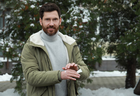 Man applying cream from tube onto hand outdoors, space for text. Winter care