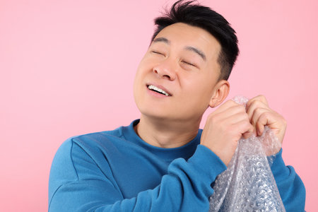 Asian man with bubble plastic wrap on pink background