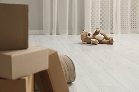 Cute lonely teddy bear on floor near boxes indoors