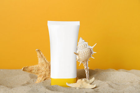 Suntan product, seashell and starfishes on sand against yellow background