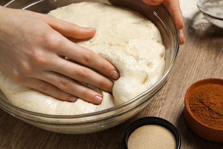 Woman kneading yeast dough for cake at wooden table, closeup