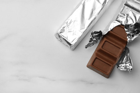 Tasty chocolate bars wrapped in foil on white table, flat lay. Space for textの写真素材