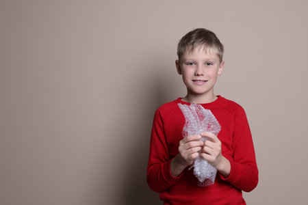 Happy boy popping bubble wrap on beige background, space for text. Stress reliefの写真素材