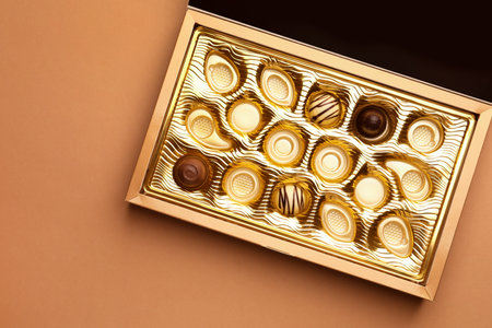 Partially empty box of chocolate candies on light brown background, top view. Space for textの写真素材