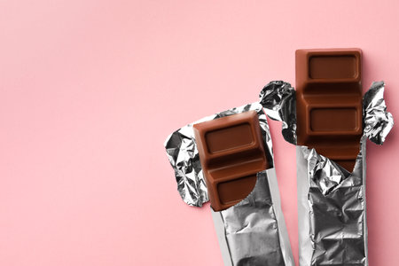 Delicious chocolate bars wrapped in foil on pink background, flat lay. Space for textの写真素材
