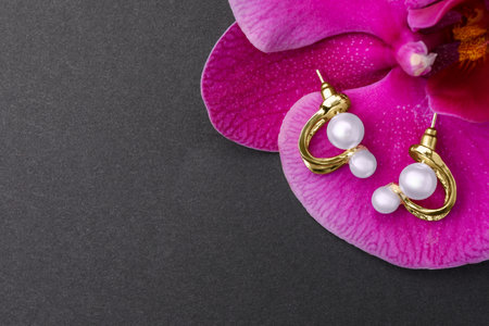 Elegant pearl earrings and orchid flower on black background, top view. Space for text