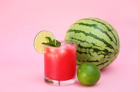 Glass of delicious watermelon drink with mint, lime and fresh fruits on pink backgroundの写真素材