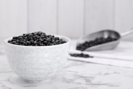 Bowl of raw black beans on white marble table. Space for text