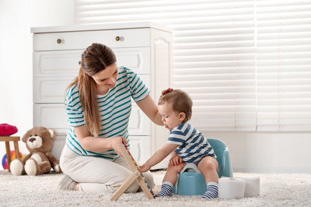 Mother training her child to sit on baby potty indoorsの写真素材