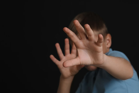 Boy making stop gesture against black background, focus on hands and space for text. Children's bullyingの写真素材