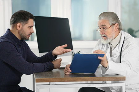Senior doctor consulting patient at wooden table in clinicの写真素材