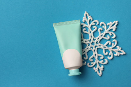 Tube of hand cream and snowflake on light blue background, flat lay with space for text. Winter skin careの写真素材