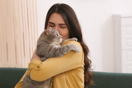 Young woman kissing her adorable cat at home, space for textの写真素材