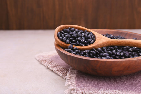 Bowl and spoon of raw black beans on light gray table, closeup. Space for text