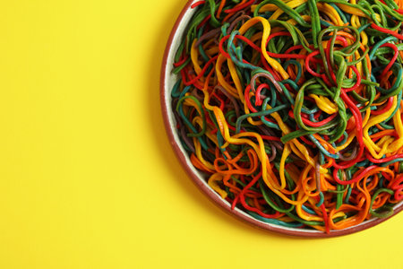 Plate of spaghetti painted with different food colorings on yellow background, top view. Space for...