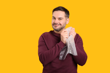 Happy asian man with bubble wrap on orange background. Space for textの写真素材
