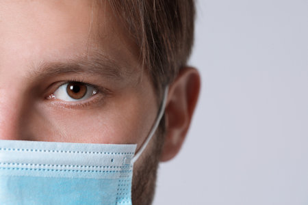 Doctor or medical assistant (male nurse) with protective mask on light grey background, closeup....