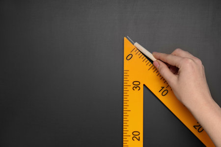 Woman drawing with chalk and triangle ruler on blackboard, closeup. Space for text