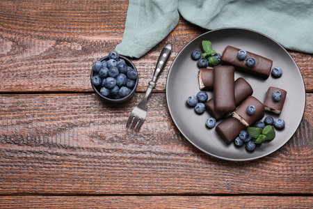 Delicious glazed curd snacks with blueberries on wooden table, flat lay. Space for textの写真素材