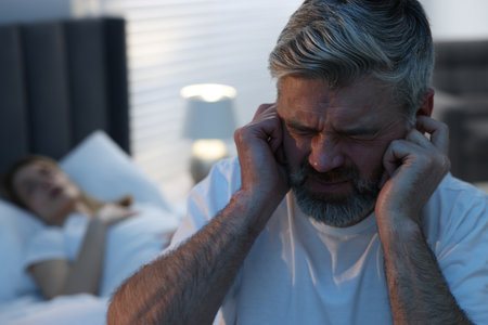 Irritated man covering his ears in bed at home, space for text. Problem with snoring wifeの写真素材