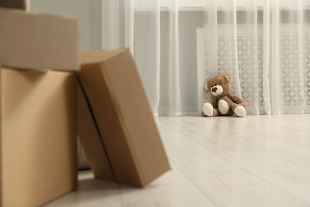 Cute lonely teddy bear on floor near boxes indoorsの写真素材