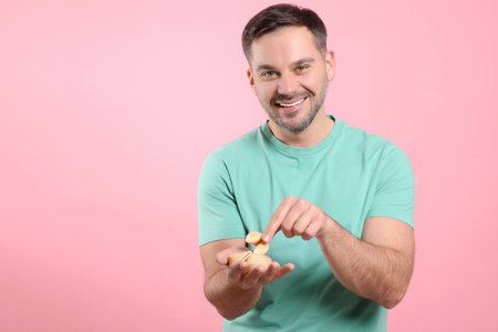 Happy man holding tasty fortune cookies with predictions on pink background. Space for textの写真素材