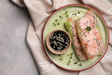 Plate with tasty spring rolls served with soy sauce on gray textured table, top view. Space for text