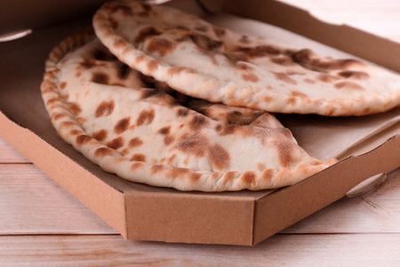 Cardboard box with delicious calzones on light wooden table, closeupの写真素材