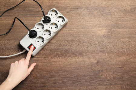 Woman pressing button of power strip on wooden floor, top view. Space for text