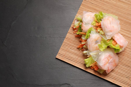 Tasty spring rolls and bamboo mat on gray textured table, top view. Space for textの写真素材