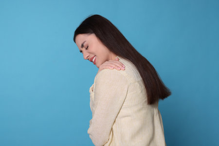 Young woman suffering from pain in shoulder on light blue background, space for text. Arthritis symptomsの写真素材