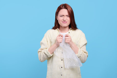 Angry woman popping wrap on turquoise background. Stress relief