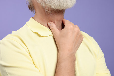 Senior man suffering from sore throat on light purple background, closeup. Cold symptomsの写真素材