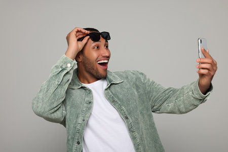 Happy African American man in sunglasses taking selfie on light gray backgroundの写真素材