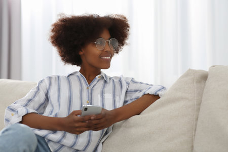 Smiling African American woman wearing glasses with smartphone at home. Space for textの写真素材