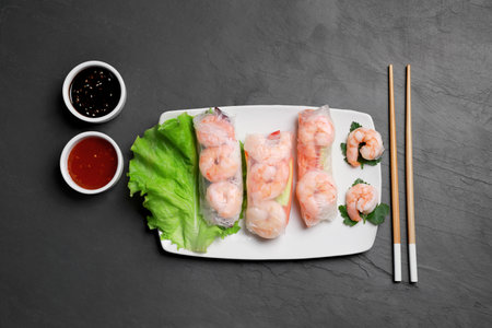 Delicious spring rolls with shrimps wrapped in rice paper served on black table, flat layの写真素材