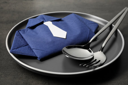 Plate with shirt made of paper napkin and cutlery on gray table, closeup. Business lunch concept