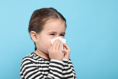 Girl blowing nose in tissue on light blue background, space for text. Cold symptomsの写真素材