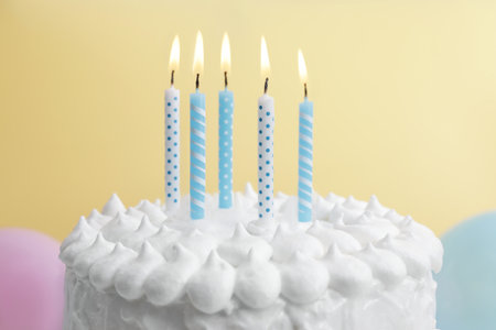 Delicious cake with cream and burning candles on yellow background, closeup