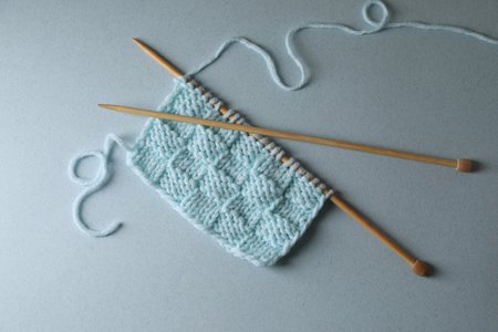 Soft turquoise knitting and needles on light blue background, top view