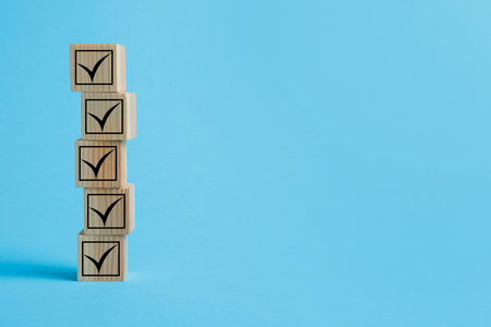 Stacked wooden cubes with check marks on light blue background. Space for textの写真素材