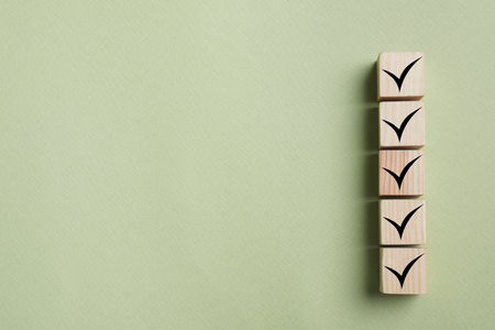 Wooden cubes with check marks on light olive color background, top view. Space for text