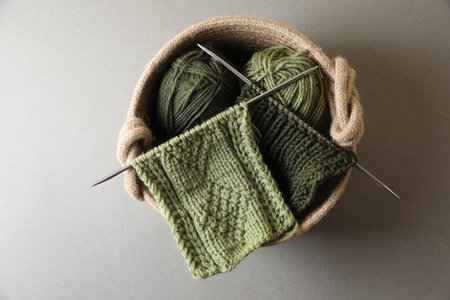 Green knitting, needles and soft yarns on light background, top view