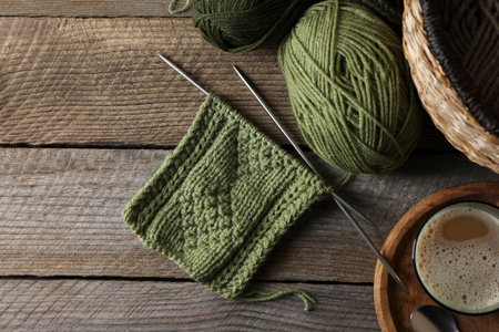 Soft green woolen yarn, knitting, needles and glass of drink on wooden table, flat lay. Space for...