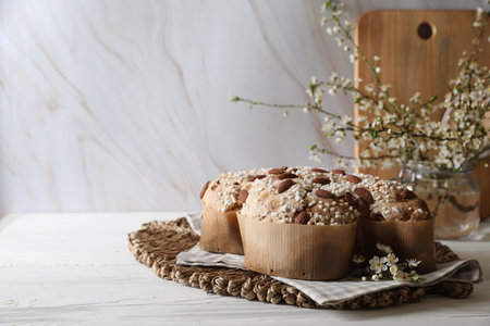 Delicious Italian Easter dove cake (Colomba di Pasqua) and flowers on white wooden table. Space for...