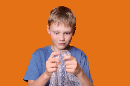 Boy popping bubble wrap on orange background. Stress reliefの写真素材