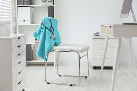 Turquoise medical uniform and stethoscope hanging on chair in clinicの写真素材