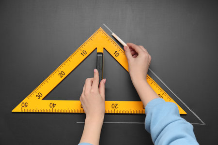 Woman drawing with chalk and triangle ruler on blackboard, closeup